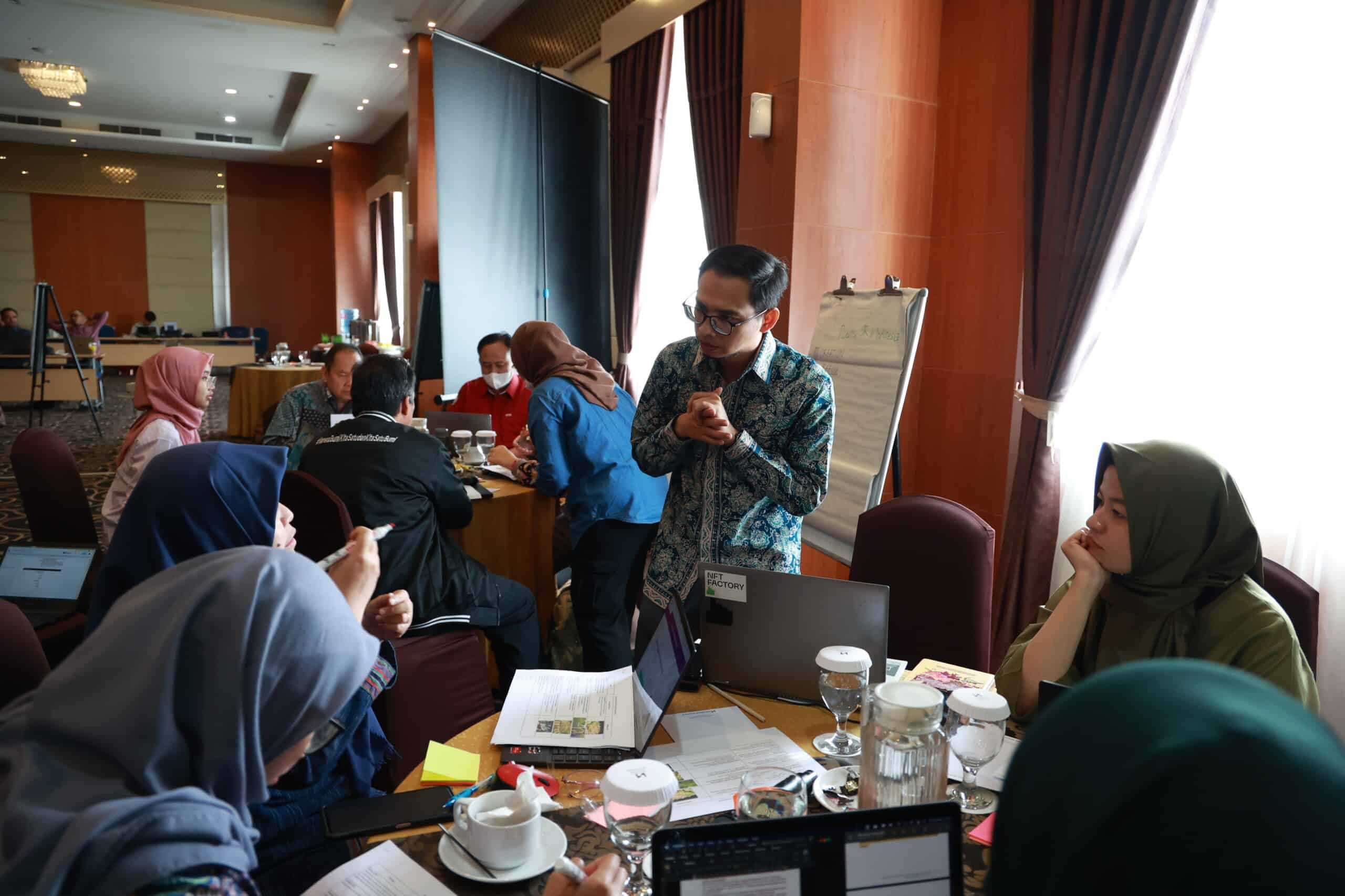 A group of people sitting around a table listening to a speaker during a workshop in Indonesia.