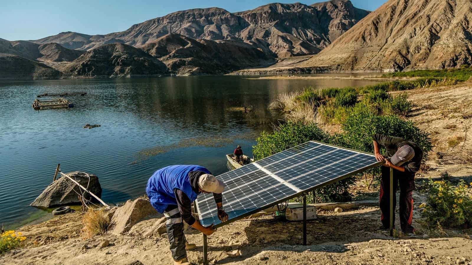 People installing solar panel by a lake in Peru mountains