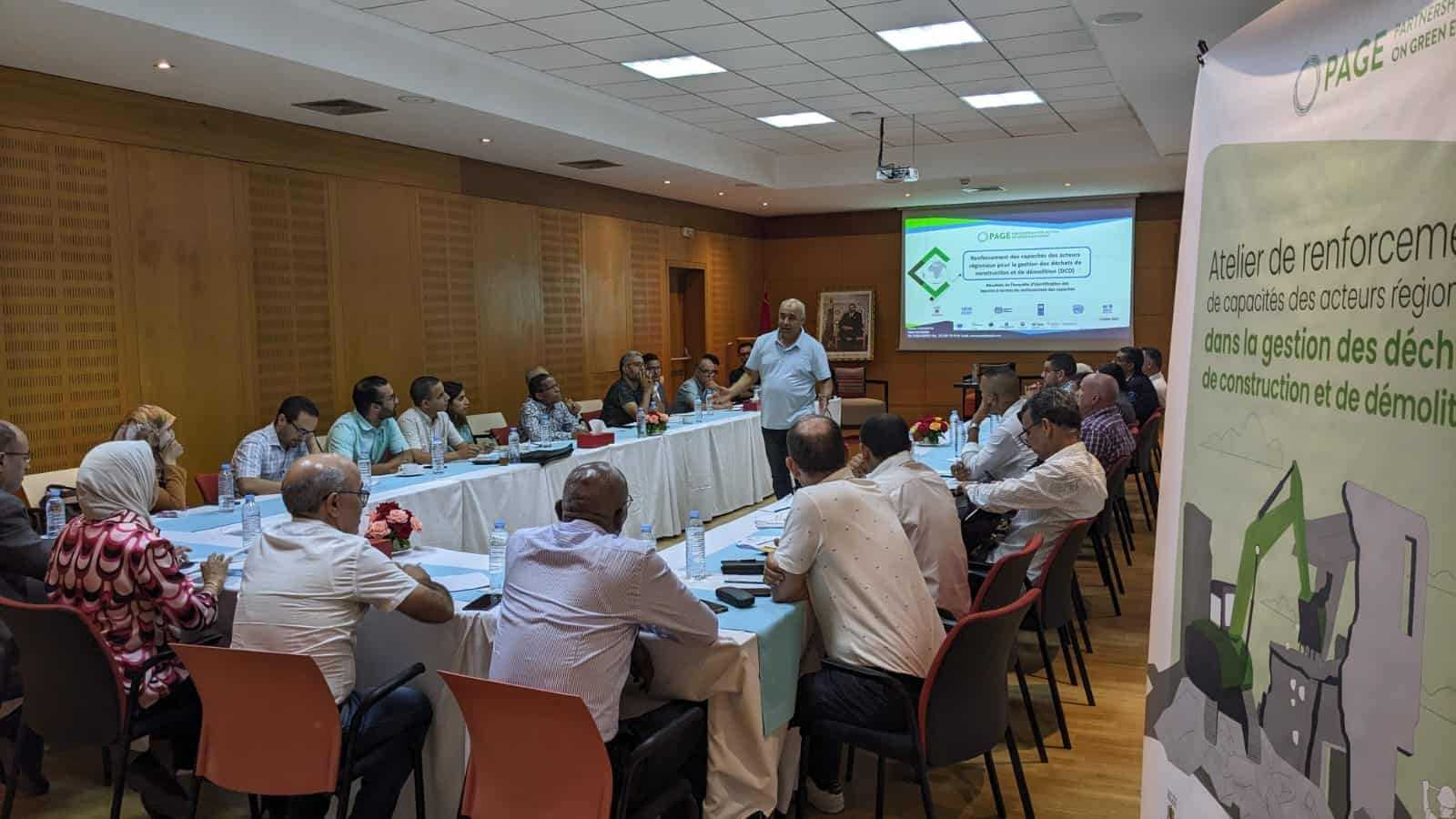 A group of people sitting at a table looking at a speaker and a screen during a workshop in Morocco.