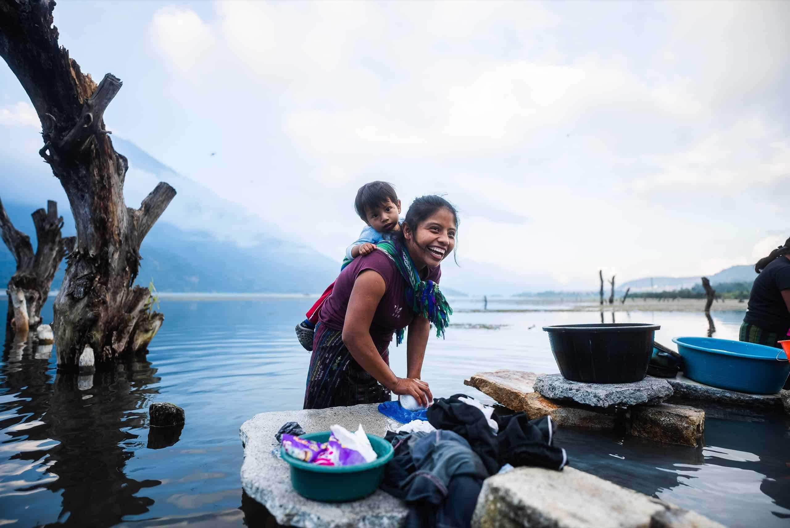 Smiling woman doing laundry with a baby on her back in Guatemala